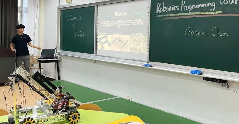 A Short Circuit member teaching robotics programming in a Taiwan classroom, with a robot on the table.